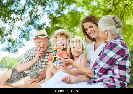 Famiglia estesa con il bambino e i nonni di mangiare il melone in giardino in estate Foto Stock