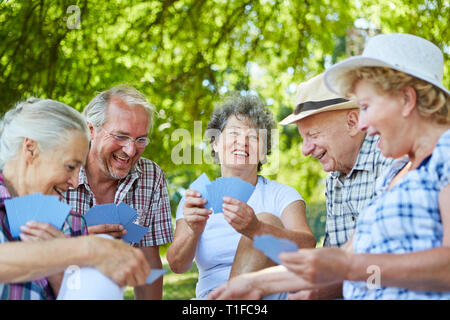 Gruppo di anziani amici giocando a carte nel parco in estate su un prato Foto Stock