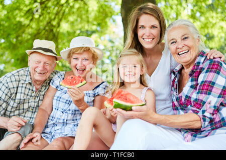 Ridendo famiglia estesa con i nonni e kid nel parco in estate mentre mangia il melone Foto Stock