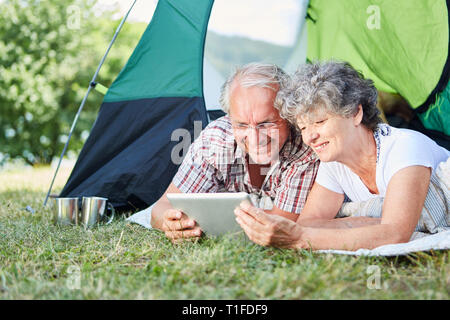 Coppia senior guarda al computer tablet in tenda durante l estate vacanze in campeggio Foto Stock