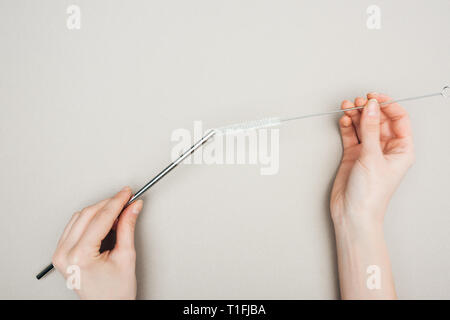 Vista parziale di donna tenendo la spazzola di pulizia e acciaio inossidabile la paglia su grigio Foto Stock