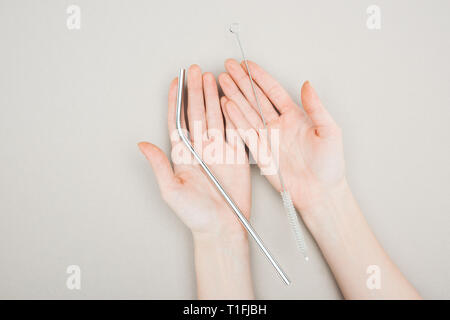 Vista ritagliata della donna tenendo la spazzola di pulizia e acciaio inossidabile la paglia su grigio Foto Stock