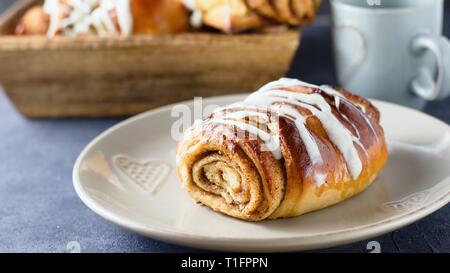 Un modo perfetto per iniziare la giornata. La colazione rustica impostazione con rotolo cannella o bun incrostato con il cioccolato bianco e la tazza di tè o caffè e alcuni più b Foto Stock