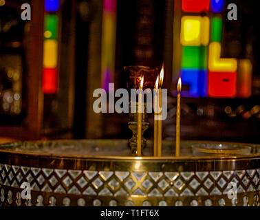 Quattro debolmente illuminata in giallo candele di cera in una Chiesa Ortodossa Greca. Immagine di stock Foto Stock