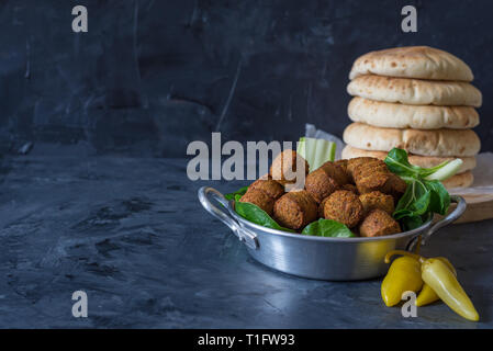 Falafel sfere servita nella piastra con foglie di colore verde e pane pita in legno su sfondo nero Foto Stock
