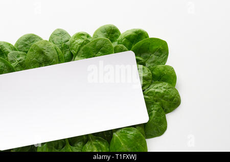 Cornice fatta di foglie di spinaci su sfondo bianco. Cucina creativa del concetto. Ingrediente per insalata. Piatto, laici vista superiore Foto Stock