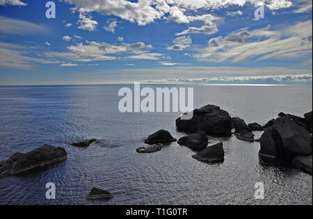 Enormi pietre nere giacciono in un mare blu su un cielo blu con nuvole bianche. La Crimea. L'Ucraina Foto Stock