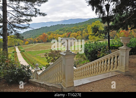 Un bianco scala di pietra in autunno giardino conduce al Giallo autunno gli alberi su uno sfondo di montagne con le nuvole di autunno Foto Stock