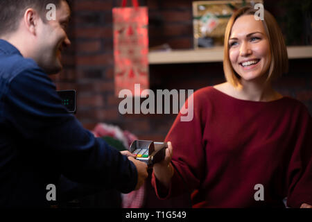 Immagine del venditore sorridente donna in piedi dietro il registratore di cassa e acquirente maschio dal retro Foto Stock