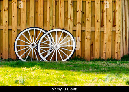 Prato verde e la recinzione di legno con due in legno bianco le ruote del carro appoggiata sulla recinzione. Foto Stock