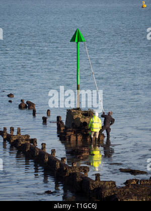 Coppia di due operai uomini lavoratori in alta vis lavora mantenendo la verniciatura riverniciatura con palo di estensione del rullo spazzola una spiaggia groyne navigazione marker Foto Stock