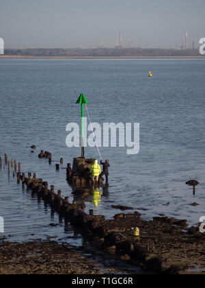 Coppia di due operai uomini lavoratori in alta vis lavora mantenendo la verniciatura riverniciatura con palo di estensione del rullo spazzola una spiaggia groyne navigazione marker Foto Stock