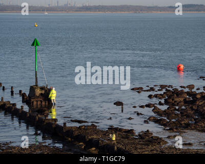 Coppia di due operai uomini lavoratori in alta vis lavora mantenendo la verniciatura riverniciatura con palo di estensione del rullo spazzola una spiaggia groyne navigazione marker Foto Stock