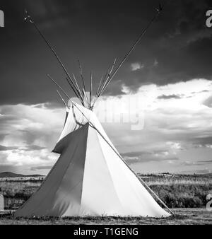 Una vista di un tende Tepee con un cielo drammatico nelle pianure occidentali al tramonto in USA in bianco e nero Foto Stock