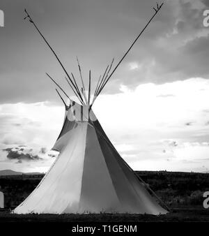 Una vista di un tende Tepee con un cielo drammatico nelle pianure occidentali al tramonto in USA in bianco e nero Foto Stock