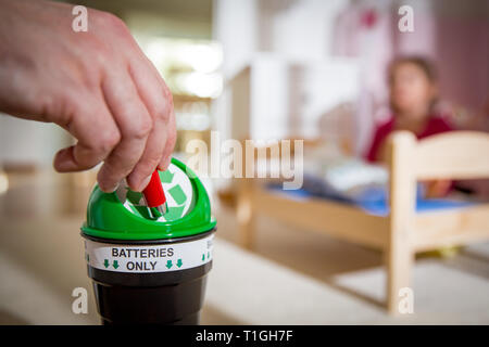 Uomo di mettere le batterie usate nella casella di riciclaggio a casa. Bambino nella nursery room giocando con i giocattoli. Separare i rifiuti nozione. Solo le batterie. Foto Stock