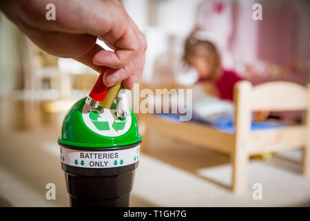 Uomo di mettere le batterie usate nella casella di riciclaggio a casa. Bambino nella nursery room giocando con i giocattoli. Separare i rifiuti nozione. Solo le batterie. Foto Stock