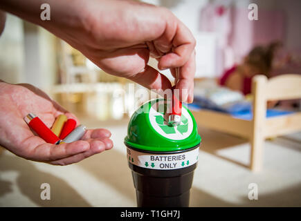 Uomo di mettere le batterie usate nella casella di riciclaggio a casa. Bambino nella nursery room giocando con i giocattoli. Separare i rifiuti nozione. Solo le batterie. Foto Stock