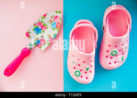 Stivali di gomma e attrezzi da giardino su sfondo lucido.bambini estate sandali e la pala con pattern di fiori.giochi dei bambini e scarponi per la spiaggia.il concetto di estate Foto Stock