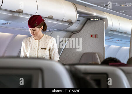 Doha, Qatar - Febbraio 20th, 2019: una femmina di equipaggio di cabina assistente di volo che parla con un passeggero a bordo su Airbus A350 della Qatar Airways. Foto Stock