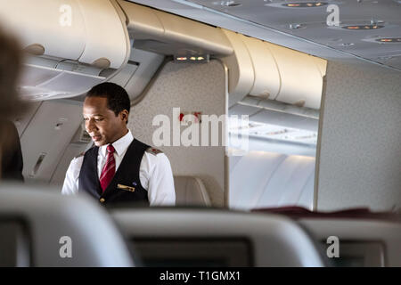 Doha, Qatar - Febbraio 20th, 2019: un maschio di equipaggio di cabina assistente di volo che parla con un passeggero a bordo su Airbus A350 della Qatar Airways. Foto Stock