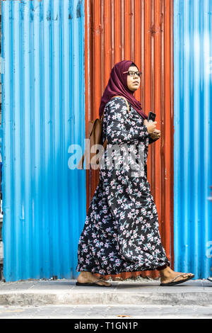 Maschio, Maldive - Febbraio 11th, 2019: una donna che indossa hijab abaya e camminare su una parete corrugata pannello nel maschio, Maldive. Foto Stock