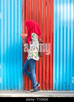 Maschio, Maldive - Febbraio 11th, 2019: una studentessa di indossare il hijab camminare su una parete corrugata pannello nel maschio, Maldive. Foto Stock