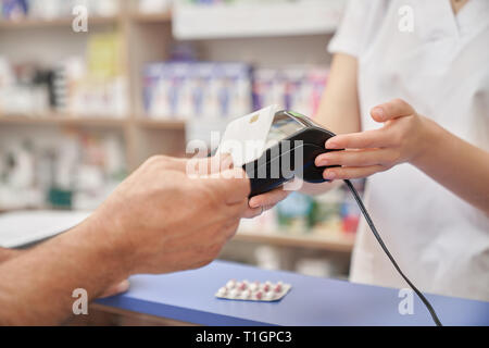 Il cliente effettuando il pagamento in farmacia. Il farmacista azienda terminale, uomo di pagare per i medicamenti con carta di credito. Pagamento moderno dalla macchina, Blister di pillole sul contatore. Foto Stock