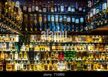 Una grande selezione di whisky scozzesi illuminata su ripiani in vetro e in ottica, Scozia Foto Stock