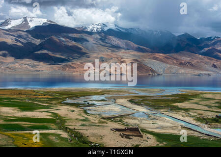 Floodplain grande lago alpino di Tso Moriri, campi verdi, blue river, nuvole nel cielo tempestoso, Himalaya. Foto Stock