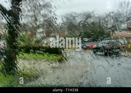Pioggia sul bagnato parabrezza auto con fuori fuoco suburban strada residenziale in background. Foto Stock