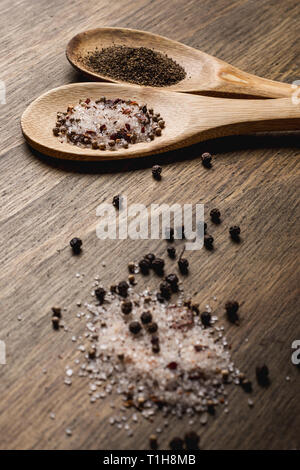 Due cucchiai di legno con sale e pepe su una tavola di legno Foto Stock