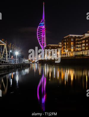 Spinnaker Tower al Gunwharf Quays Portsmouth illuminato di viola di notte per epilessia nazionale giorno riflettendo sull'acqua Foto Stock