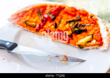 Primo piano della crosta di fresco in casa vegan fette di pizza coltello per metà sul tavolo in Italia con salsa di pomodoro rosso verdura consumate Foto Stock