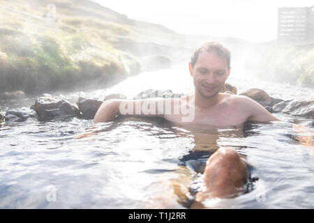 Uomo di balneazione in Hveragerdi Reykjadalur sorgenti calde durante la stagione autunnale mattinata giorno nel sud dell'Islanda su golden circle rocce e vapore di fiume Foto Stock