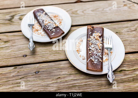 Primo piano di due crêpe al cioccolato dessert si avvolge con scaglie di noce di cocco realizzato in essiccatore con banane su piastre e forche Foto Stock