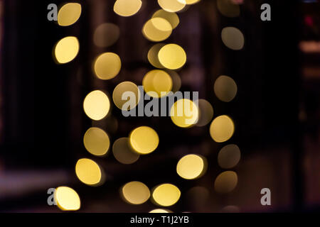 Round bokeh astratta con sfondo giallo golden cerchi illuminato luci di decorazione su albero di notte scura sera di Natale nero Foto Stock