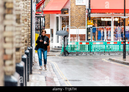 London, Regno Unito - 12 Settembre 2018: Donna gente camminare con ombrelloni in città piovosa meteo sul marciapiede strada bagnata riflessione shopping a SoHo Foto Stock