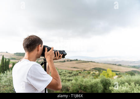 Val D'Orcia campagna in Toscana, Italia, con il verde delle colline con la fattoria del paesaggio e giovane fotografo turistico di scattare una foto con la fotocamera Foto Stock