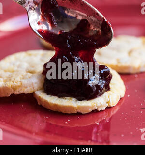 Mangiare marmellata di prugne su una targhetta rossa con il Mais / biscotti di riso Foto Stock
