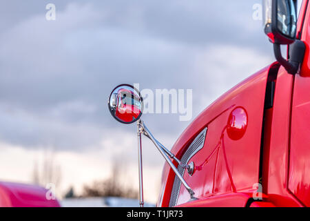 La cabina del rosso professionale di grado industriale big rig semi permanente del carrello sul lotto di parcheggio nei pressi di magazzino è riflessa nella rotonda vista posteriore mir Foto Stock