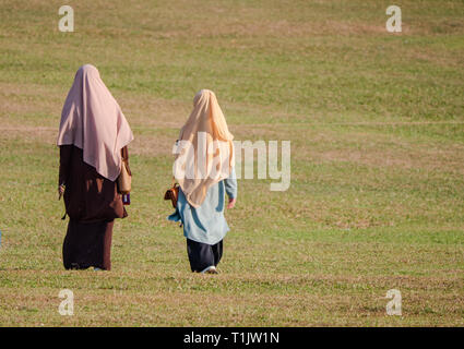 Due donne Musulmane di indossare abiti tradizionali di camminare su un campo in Johor Stato della Malaysia. Foto Stock