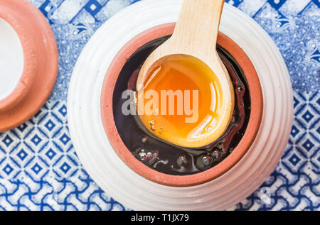 Materie africana di miele in una ceramica honey pot con il cucchiaio di legno su etnica panno blu Foto Stock