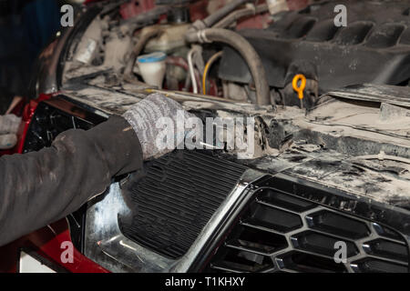 La mano di un uomo a mettere su o il distacco del paraurti anteriore da un rosso auto moderna in un veicolo officina di riparazione. Industria in auto service. Foto Stock