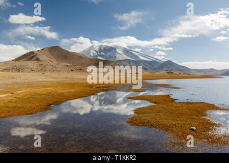 Vista sul Muztagh Ata / Muztagata montagna, una delle più alte vette del Pamir Mountains. Le acque di fronte la montagna appartengono al Lago Karakul. Foto Stock