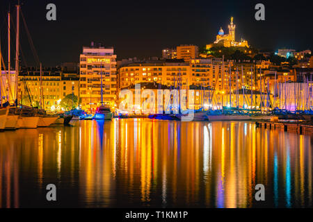 Marseille, Francia durante la notte. Il famoso porto europeo vista sulla cattedrale di Notre Dame de la Garde con colorati riflesso nell'acqua Foto Stock