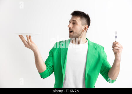 Giovani sorridente attraente ragazzo caucasico tenendo piatto vuoto e la forcella isolato su sfondo grigio. Spazio di copia e mock up. Modello vuoto dello sfondo. Foto Stock