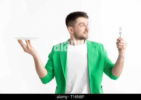 Giovani sorridente attraente ragazzo caucasico tenendo piatto vuoto e la forcella isolato su sfondo grigio. Spazio di copia e mock up. Modello vuoto dello sfondo. Foto Stock