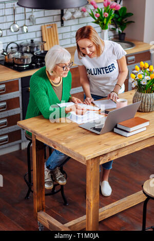 Volontario sorridente ragazza che lavora con il bianco-pelose granny su progetto di prestito Foto Stock