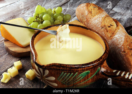 Gourmet fonduta svizzera cena su una sera d'inverno con formaggi assortiti su una scheda a fianco di una pentola riscaldata della fonduta di formaggio con due forchette intingere il pane Foto Stock